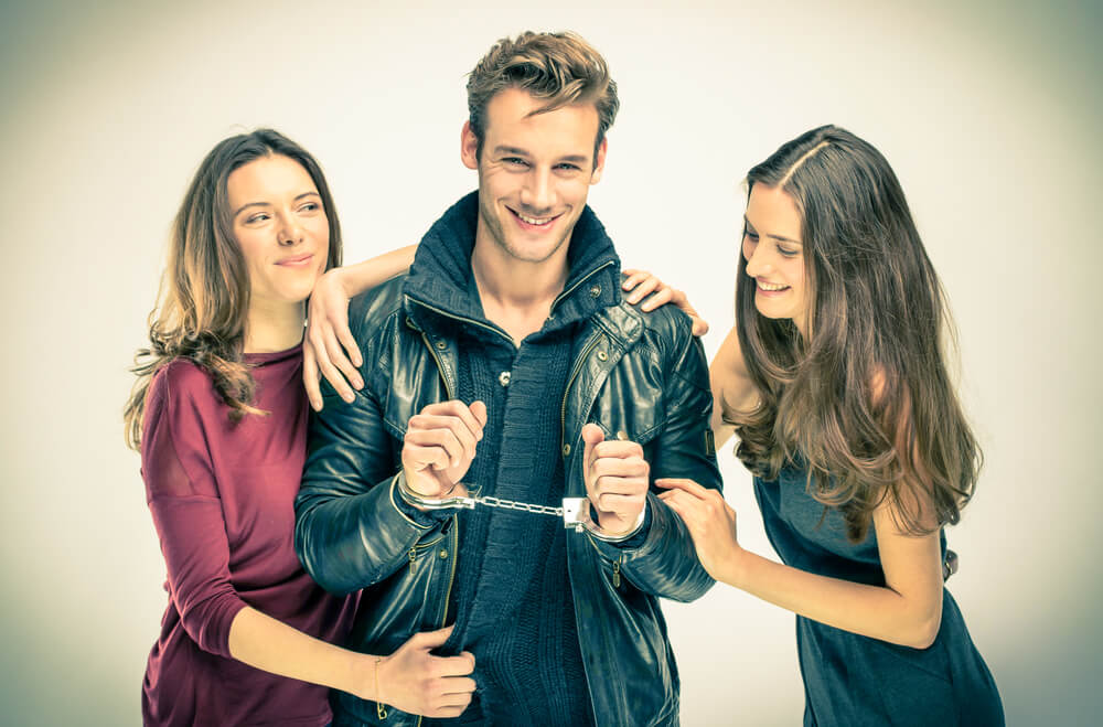 Two good looking women with a hot guy handcuffed. Three of them are all smiling.