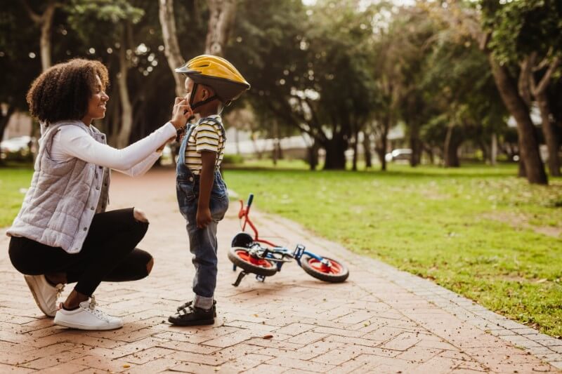 single mother helps her son with his helmet while he learns to drive a bike