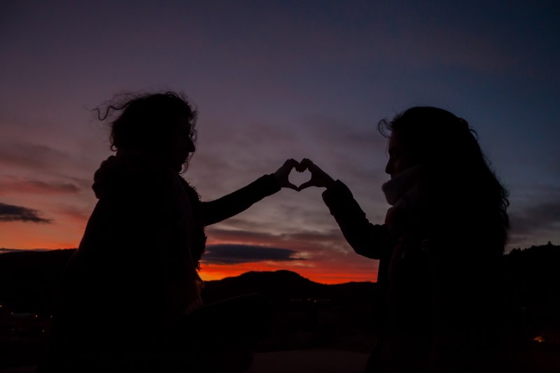 two people forming a heart with their hands in the sunset