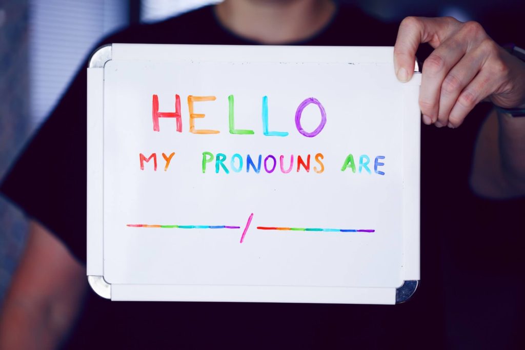 someone holding up board that says "hello my pronouns are none"